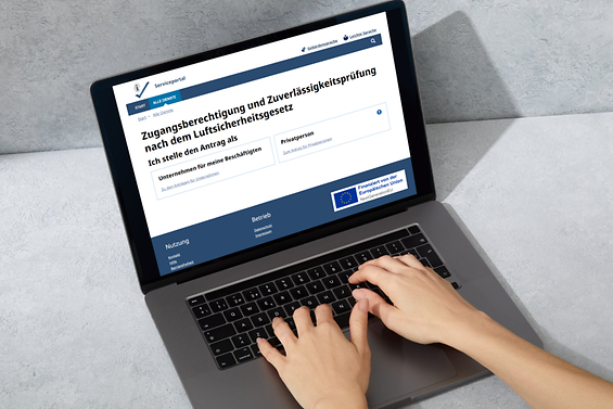 Der Online-Dienst ist auf einem Laptop-Display geöffnet, Hände tippen in der Tastatur.